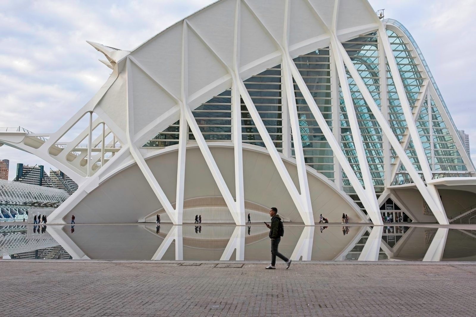 Auto-generated description: A person walks in front of a modern architectural structure with geometric shapes and reflective surfaces.
