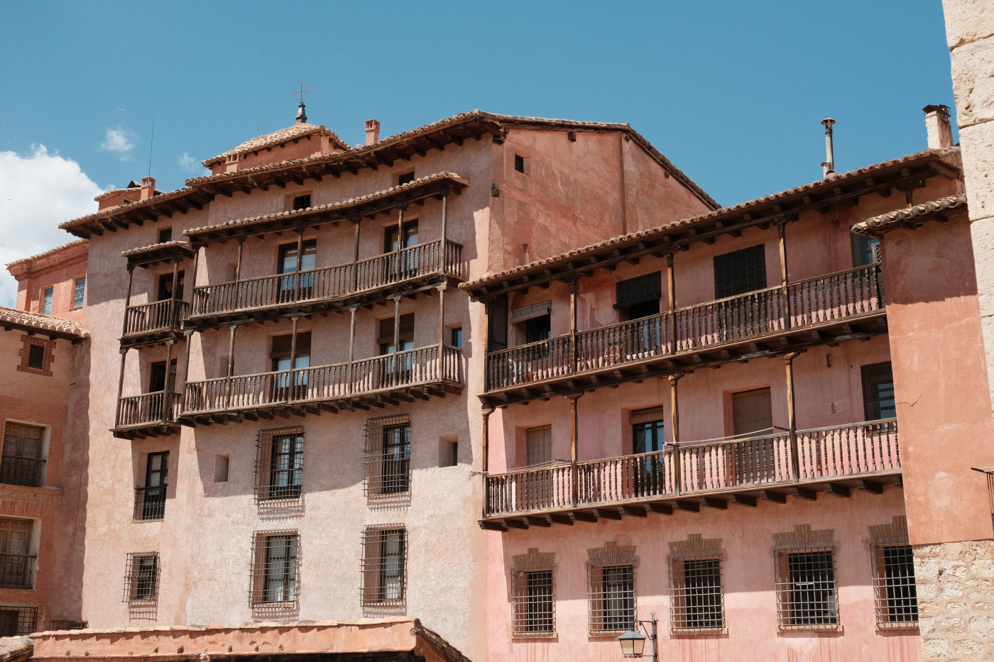 Auto-generated description: A historic building with wooden balconies and pink-hued walls stands against a clear blue sky.