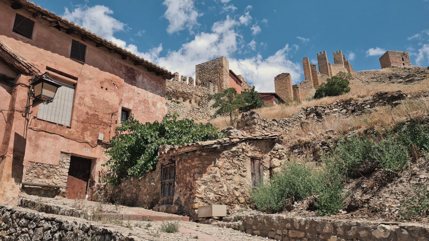 Auto-generated description: A rustic hillside reveals an ancient stone structure with rugged walls under a clear blue sky.