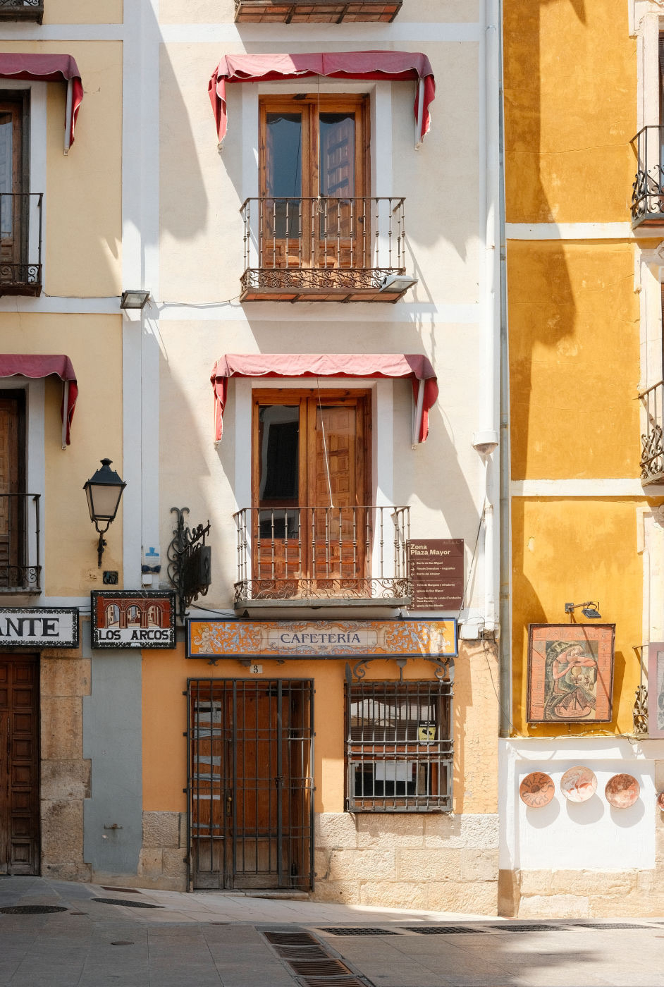 Auto-generated description: A charming building facade features small balconies, a cafeteria entrance, and warm yellow and white tones.