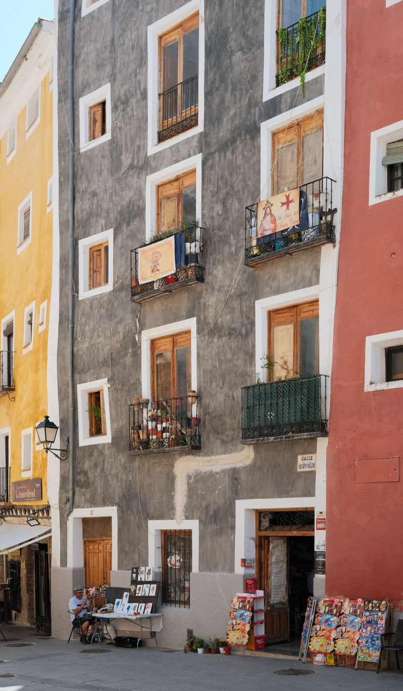 Auto-generated description: A colorful street scene features an assortment of storefronts and art displays in front of a tall, multi-story building with balconies.